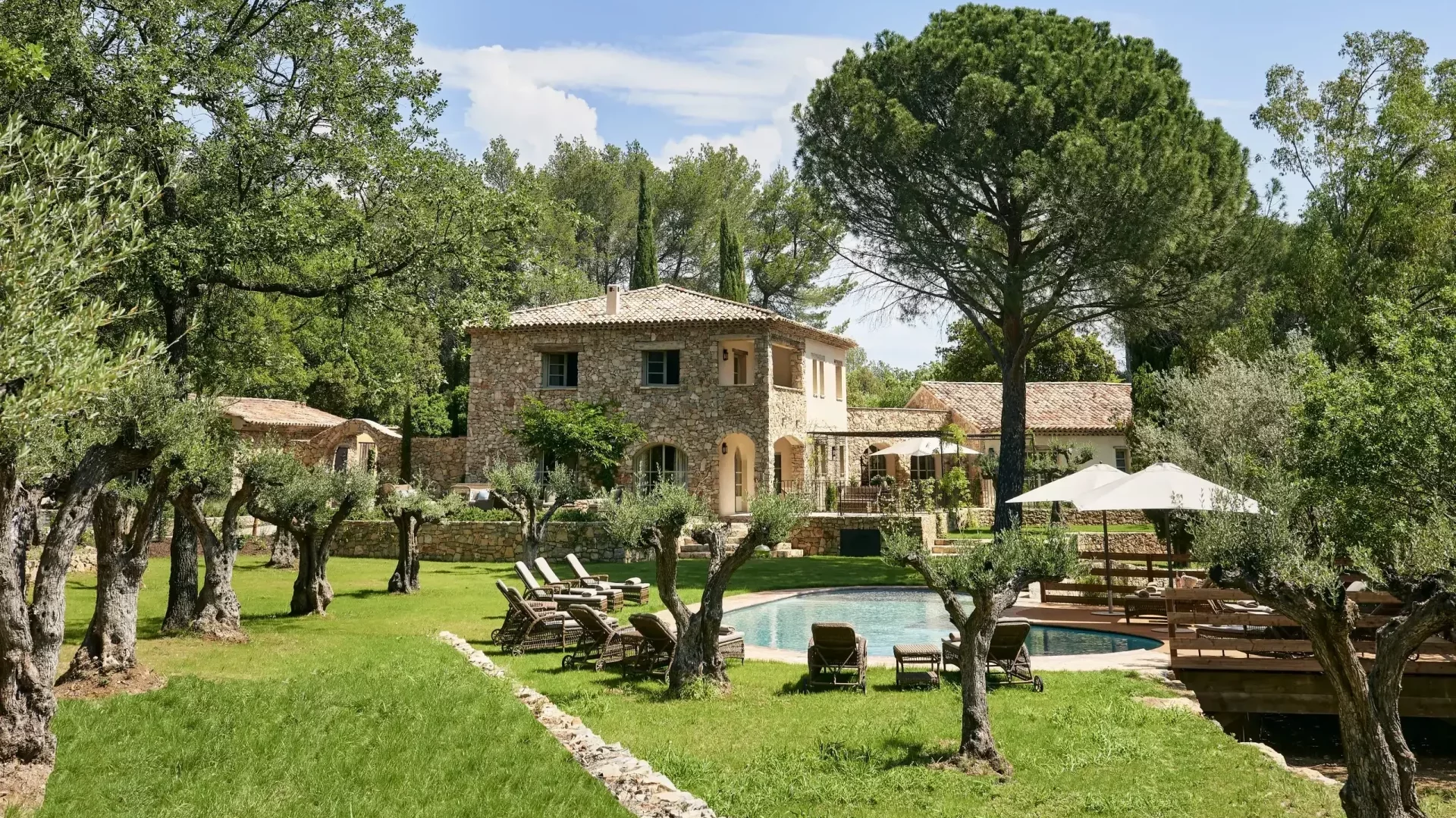 Vue extérieure de la Villa Vanado au château de Berne avec la piscine, les oliviers et les chaises longues.