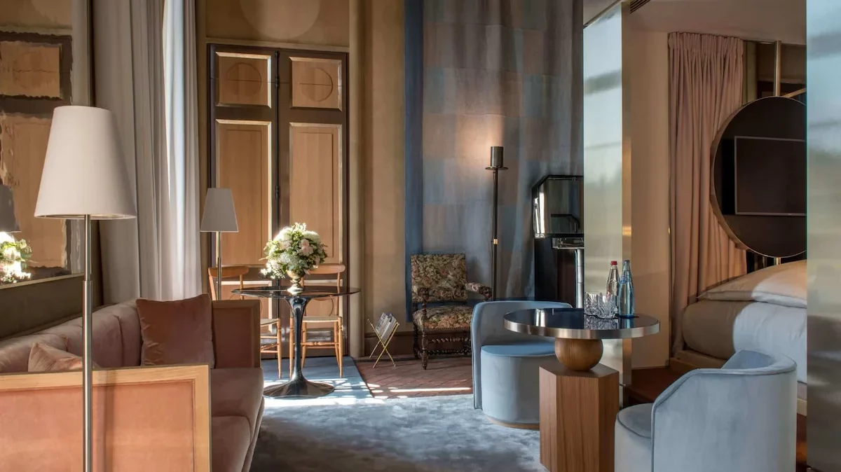 Chambre chic avec canapé rose, table en verre, rideau bleu, portes bois foncé, chaises modernes au Cours des Vosges à Paris.
