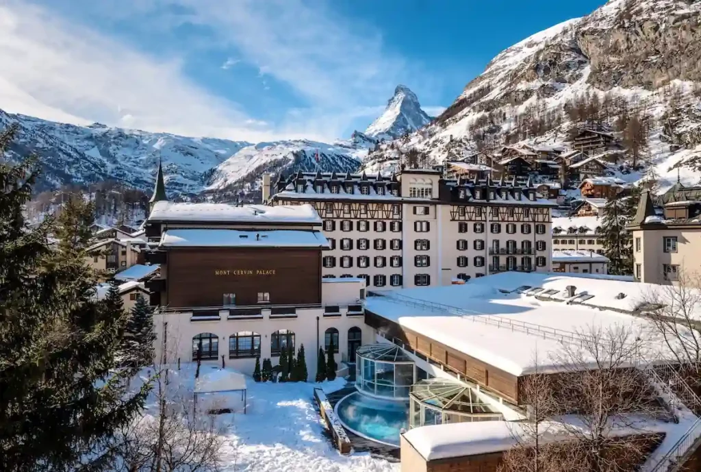 Vue extérieure sur la façade majestueuse du Mont Cervin Palace en hiver avec le mont Cervin enneigé en arrière-plan.
