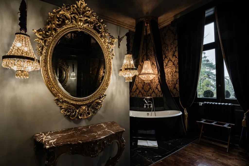 Salle de bains de la chambre Carnaval à Venise au Château de Maubreuil : baignoire îlot noire, miroir doré baroque et lustres à pampilles.