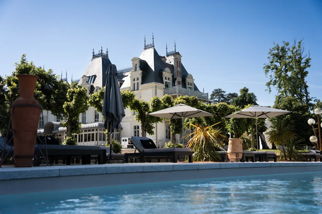 Piscine extérieure du Château de Maubreuil et façade du château sous un ciel bleu, transats et jarres en terre cuite au premier plan.