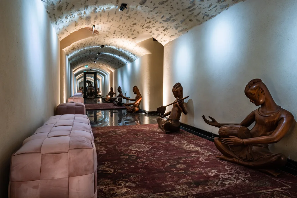 Couloir du spa Cinq Mondes du Château de Maubreuil dans les caves voûtées : statues de musiciens en bois sculpté, tapis d'Orient et banquettes de velours rose.