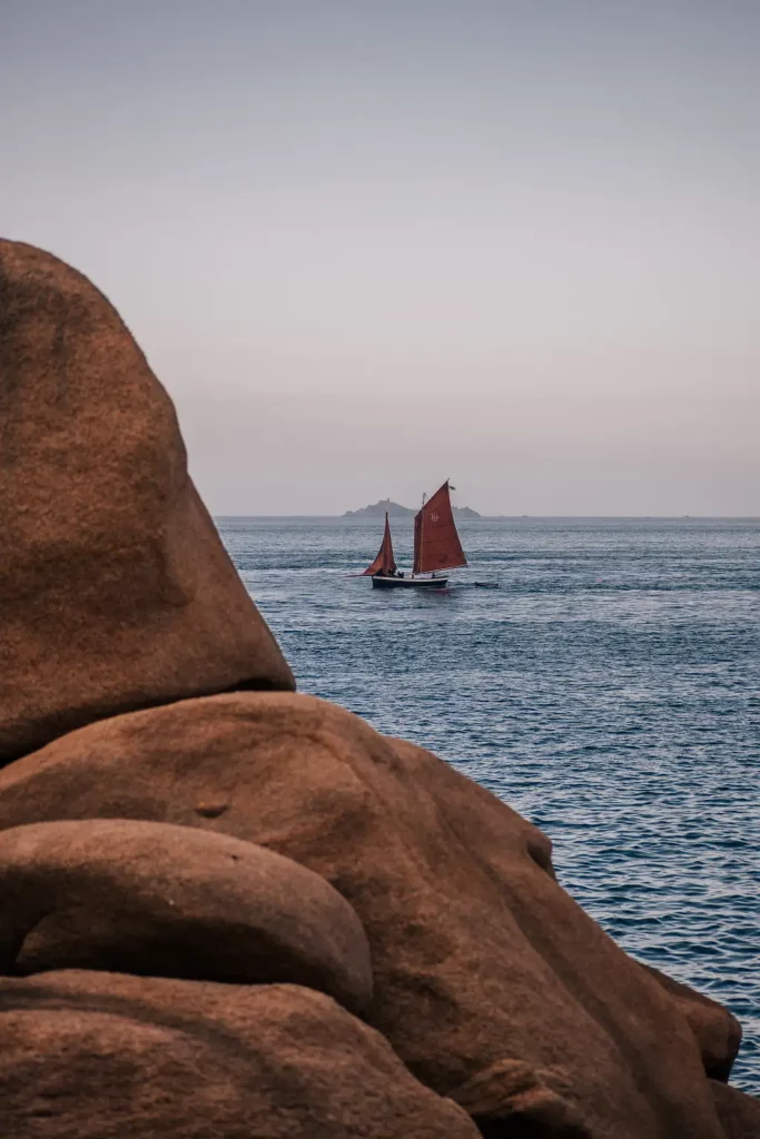 Au large de l'hôtel Les Bassans, un vieux gréement aux voiles rouges longe la Côte de Granit Rose face aux Sept-Îles, à Perros-Guirec.