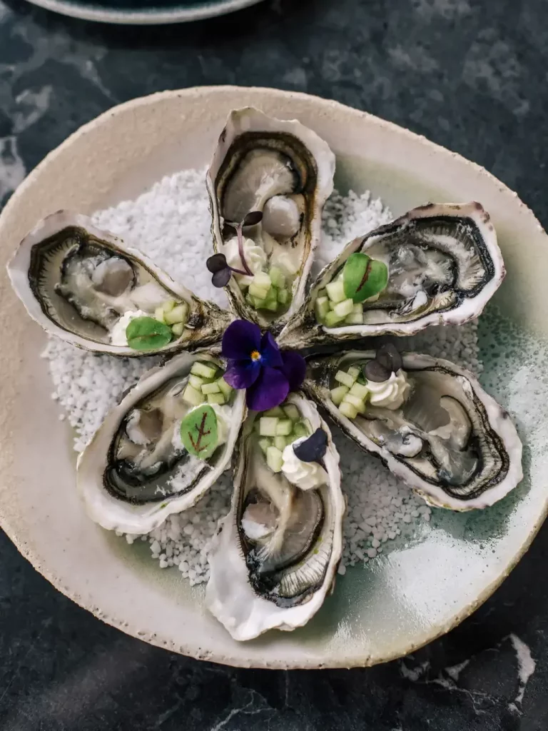 Assiette d'huîtres dressées en rosace au restaurant de l'hôtel Les Bassans, fleur comestible et brunoise de concombre, cuisine iodée du restaurant.