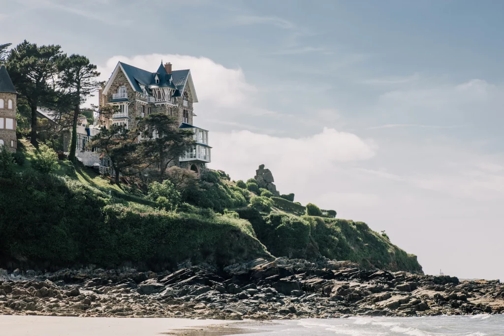 L'hôtel Les Bassans, ancien Manoir du Sphinx, vu depuis la plage de Trestrignel : pierre et toits d'ardoise dominant les rochers.