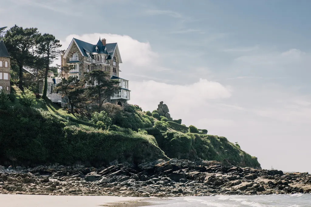 L'hôtel Les Bassans, ancien Manoir du Sphinx, vu depuis la plage de Trestrignel : pierre et toits d'ardoise dominant les rochers.