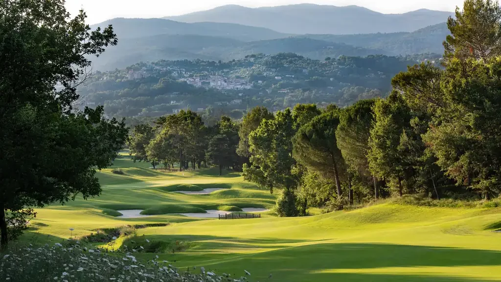 Parcours de golf de Terre Blanche au coucher du soleil, fairways vallonnés face à un village perché du haut Var