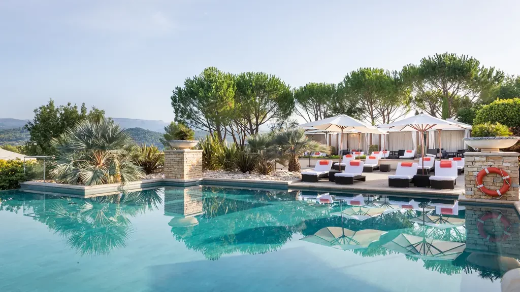 Piscine extérieure de Terre Blanche encadrée de pins parasols, transats et parasols
