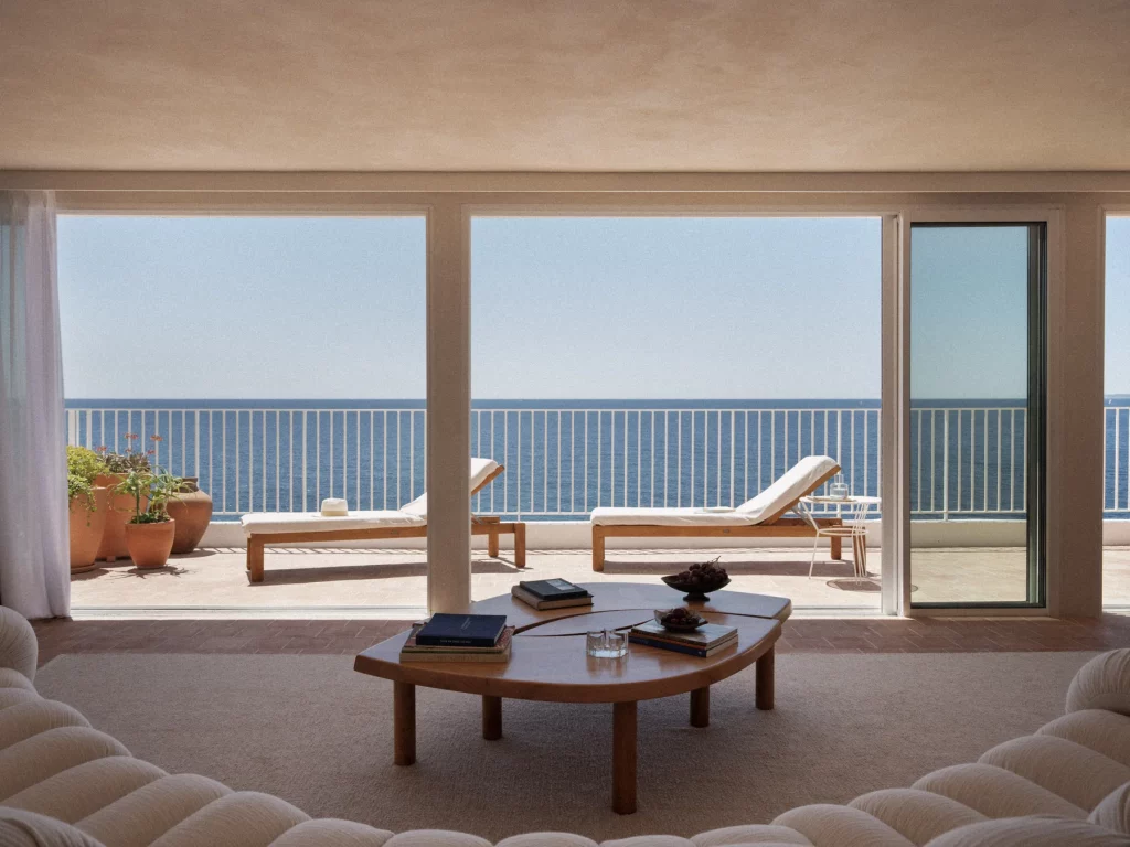 Les baies de la Suite Riviera des Roches Rouges cadrent la Méditerranée, transats en bois sur la terrasse et table basse en bois à l'intérieur.