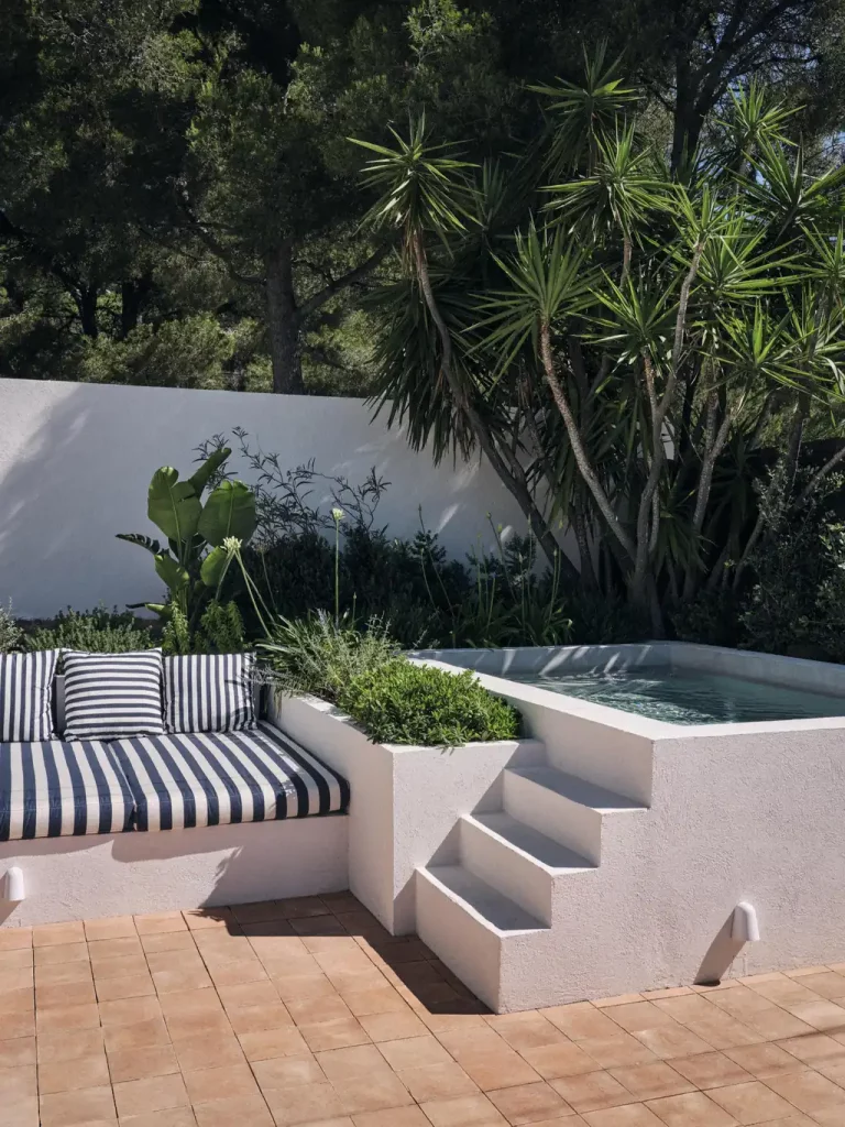 Terrasse des Roches Rouges avec bassin encastré, banquette maçonnée à coussins rayés et jardin méditerranéen planté de yuccas.