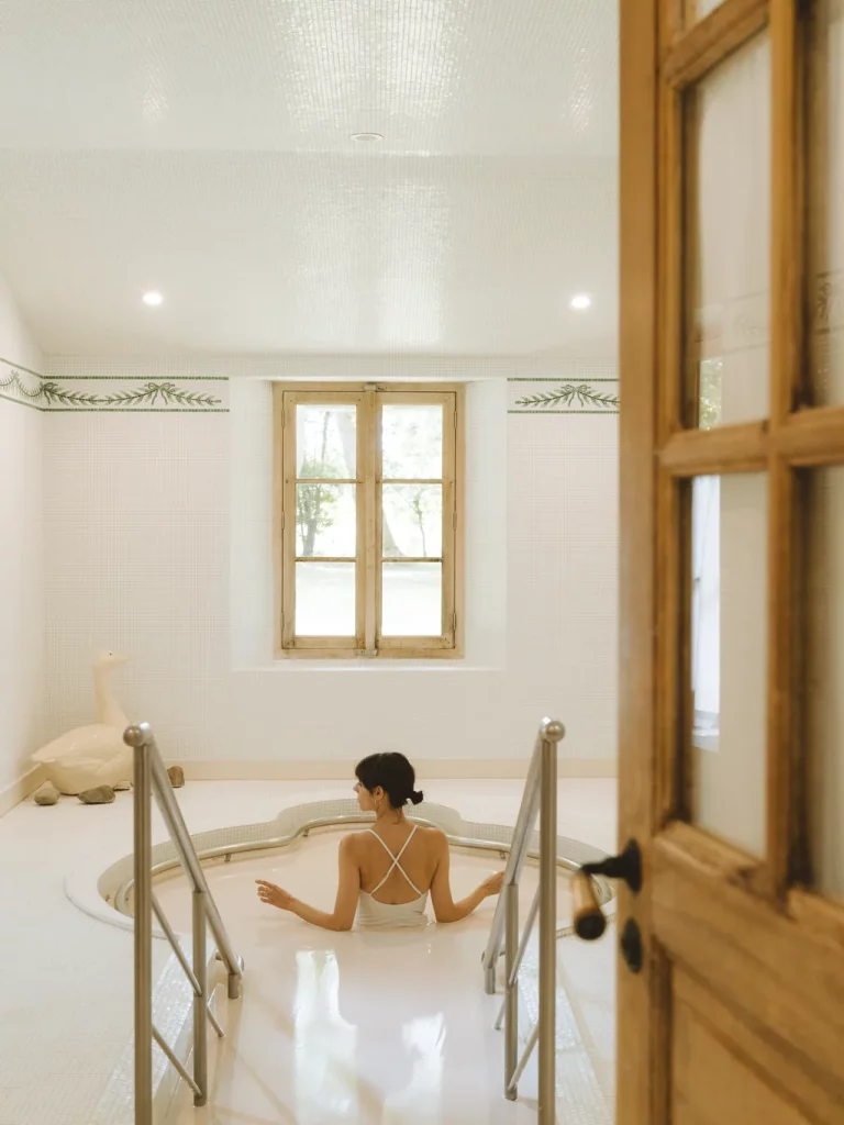 Une baigneuse dans le bain de kaolin de la Ferme Thermale des Prés d'Eugénie, pièce carrelée de blanc à frise de fougères.