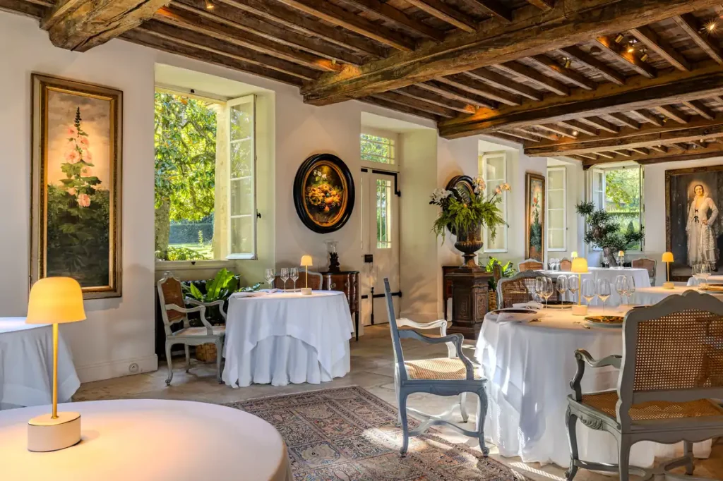 La salle du restaurant Michel Guérard aux Prés d'Eugénie, tables nappées de blanc sous une charpente ancienne, décor Second Empire.