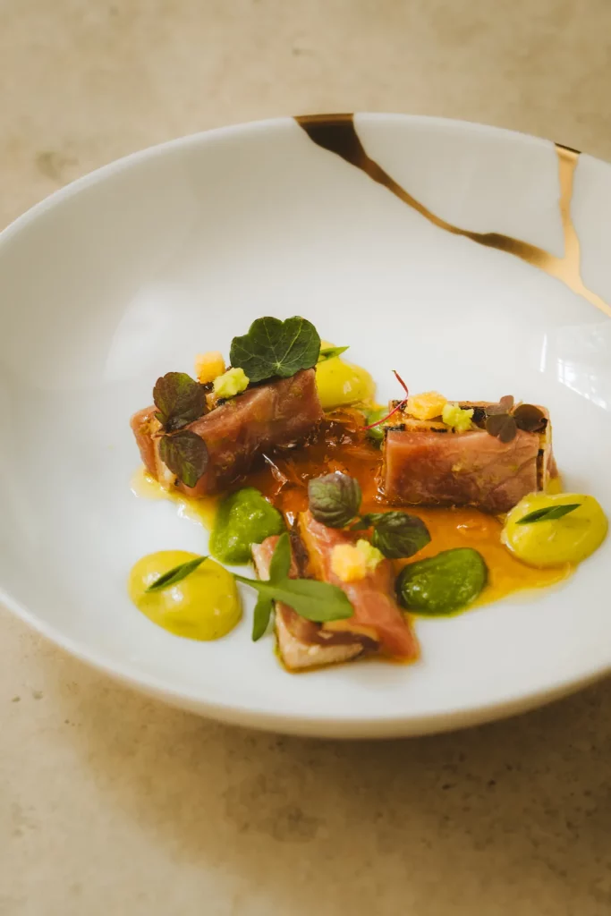 Ventre de thon et foie gras saisis sur les braises, purées d'herbes et feuilles de capucine, dans une assiette blanche veinée d'or au restaurant Michel Guérard des Prés d'Eugénie.