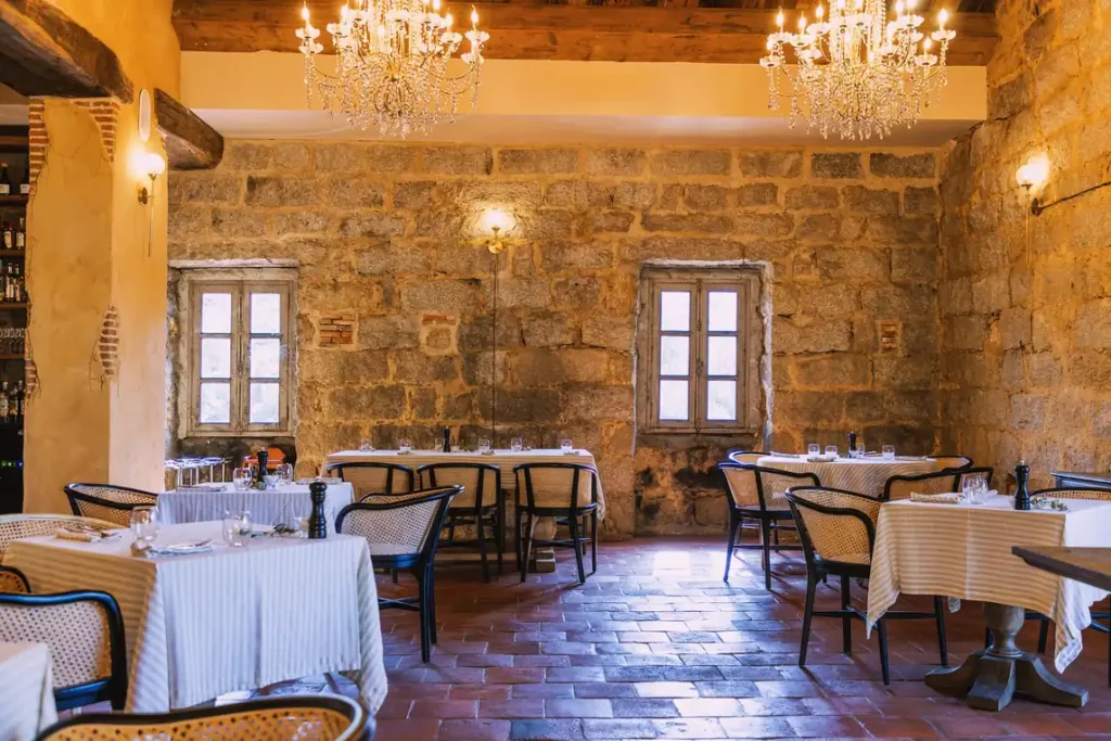 Salle du restaurant Sopravigna au Hameau de Saparale, murs de granit, lustres en cristal et tables dressées.